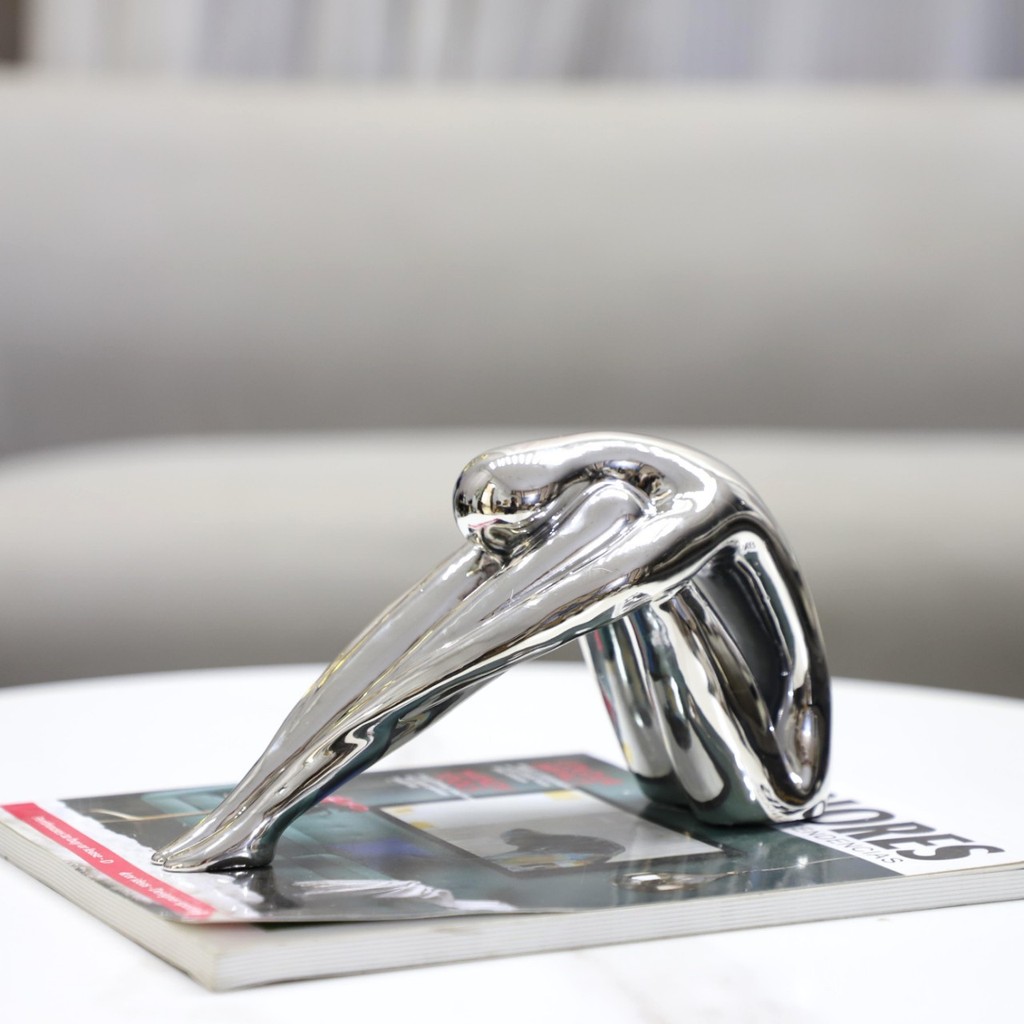 A1JV European-style, minimalist abstract electroplated resin silver sculpture of a figure hugging its knees, a small dec